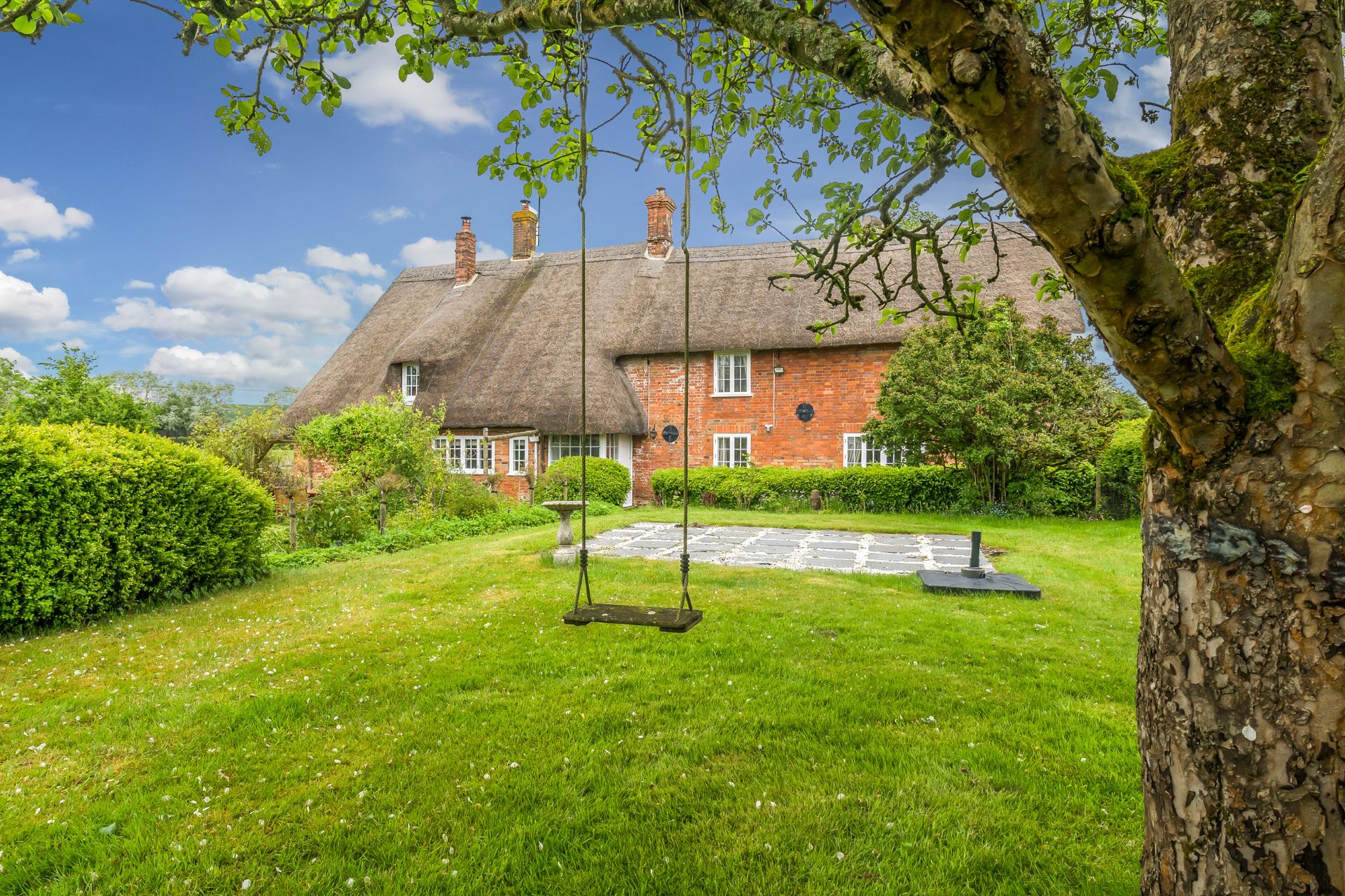 Thatched red brick cottage with lawns and a swing.