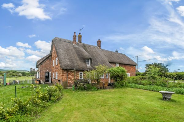 Thatched red brick cottage with lawns in the foreground.