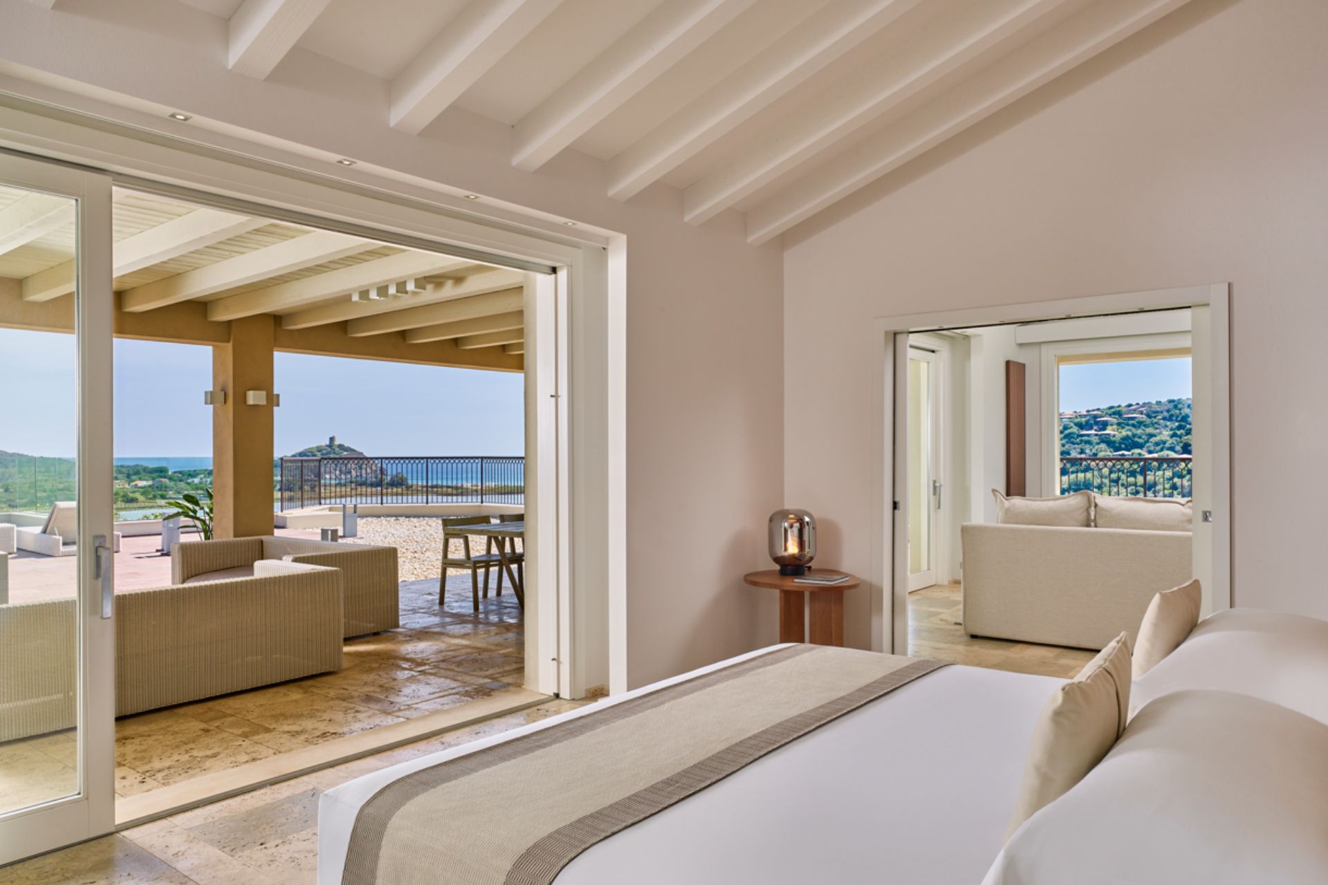 Bedroom with cream walls, white bed linens and a balcony overlooking the Sardinian mountains.