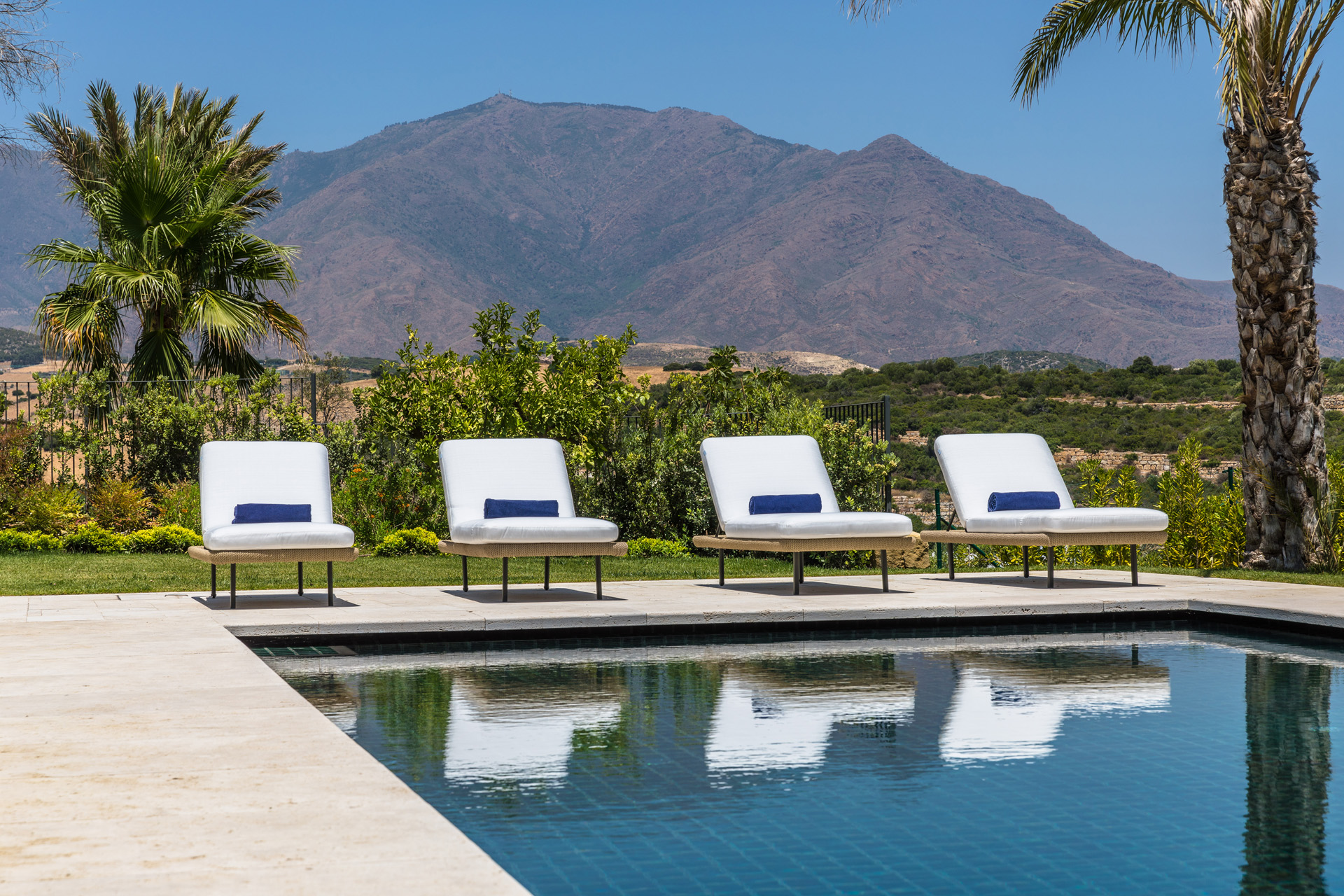 Four sunbeds by the pool with a mountain in the background
