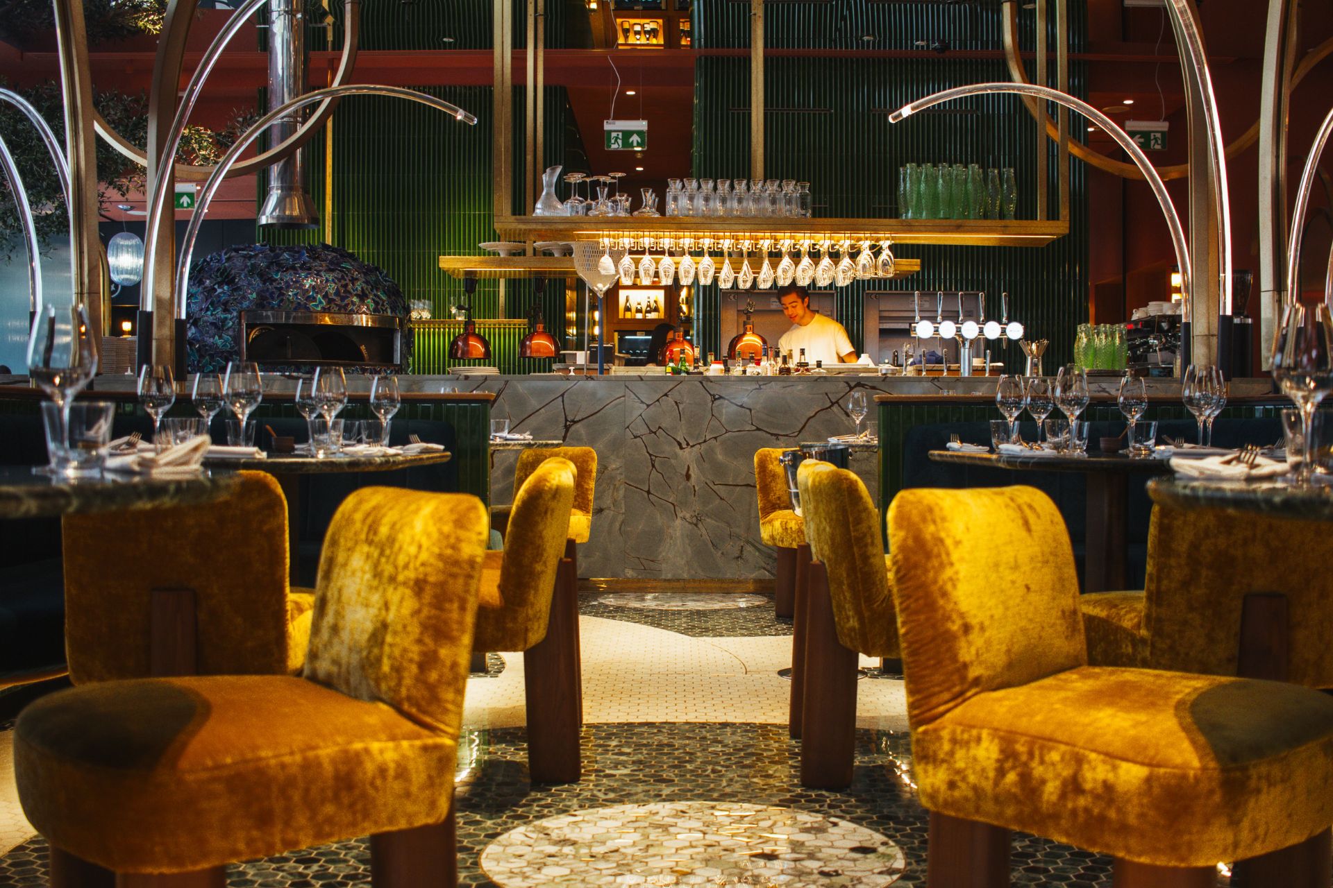 Restaurant with yellow crushed velvet seats, marble tables and a central bar.