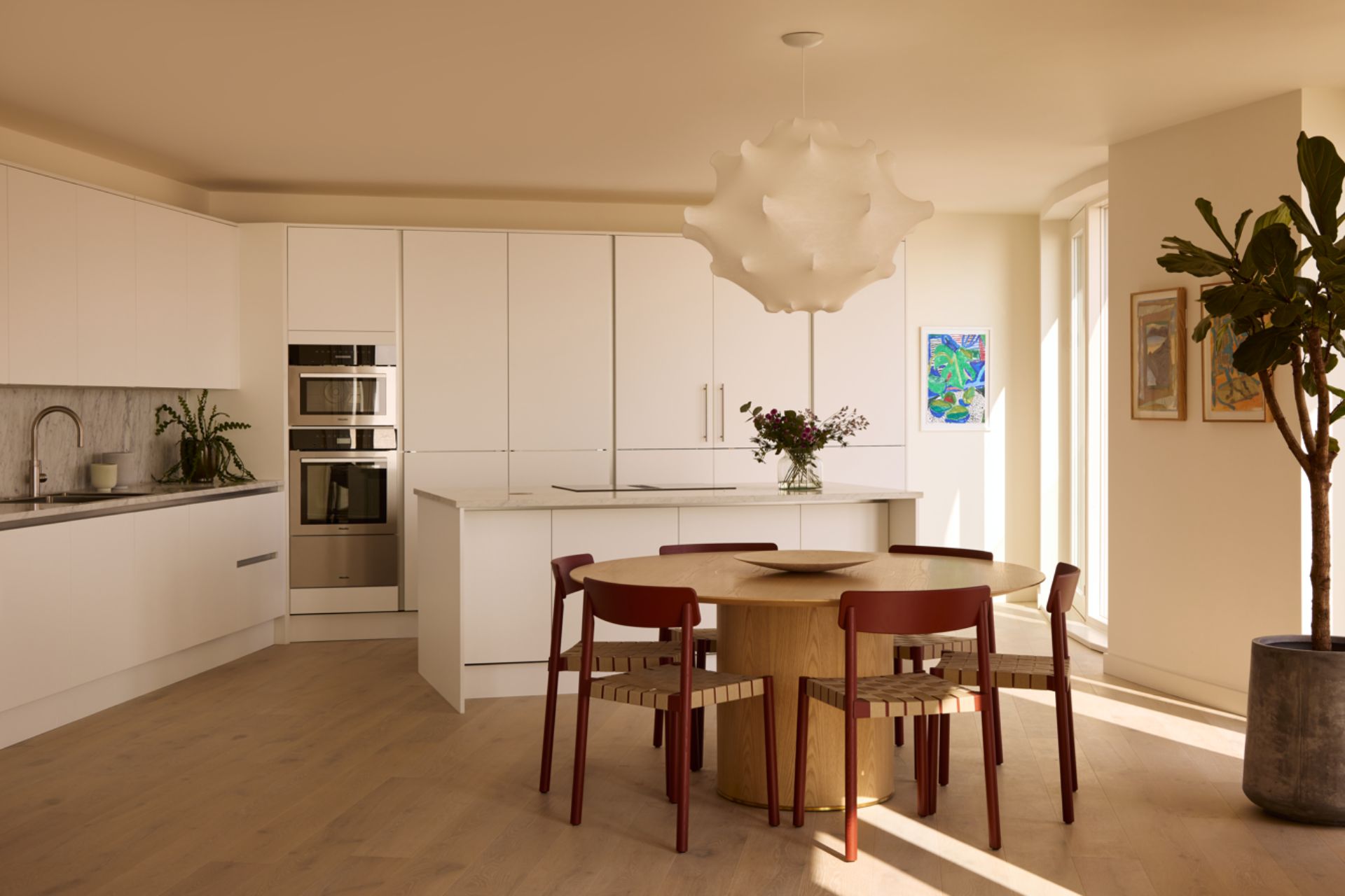 Kitchen with white cabinets, a circular wooden dining table and a white pendant light.