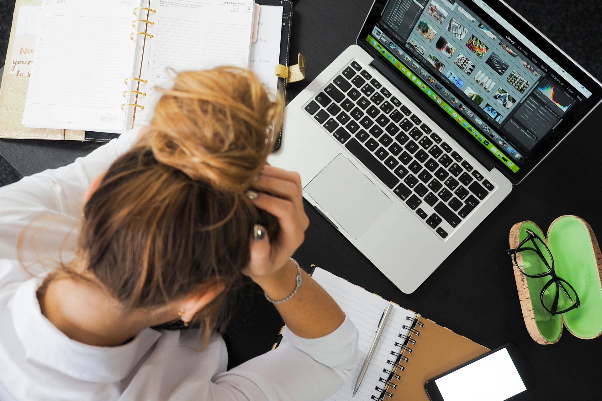 A woman holding her head beside a laptop and notebook
