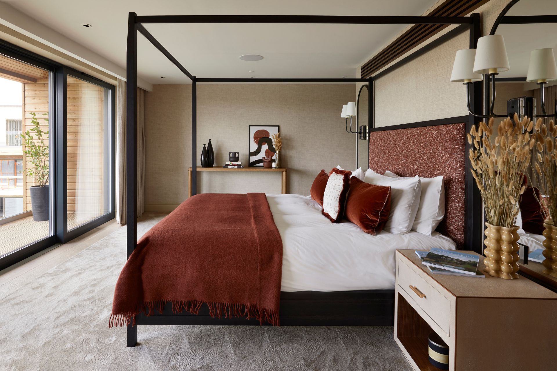 Bedroom with black-framed four poster bed, burnt orange accents, and wooden bedside tables