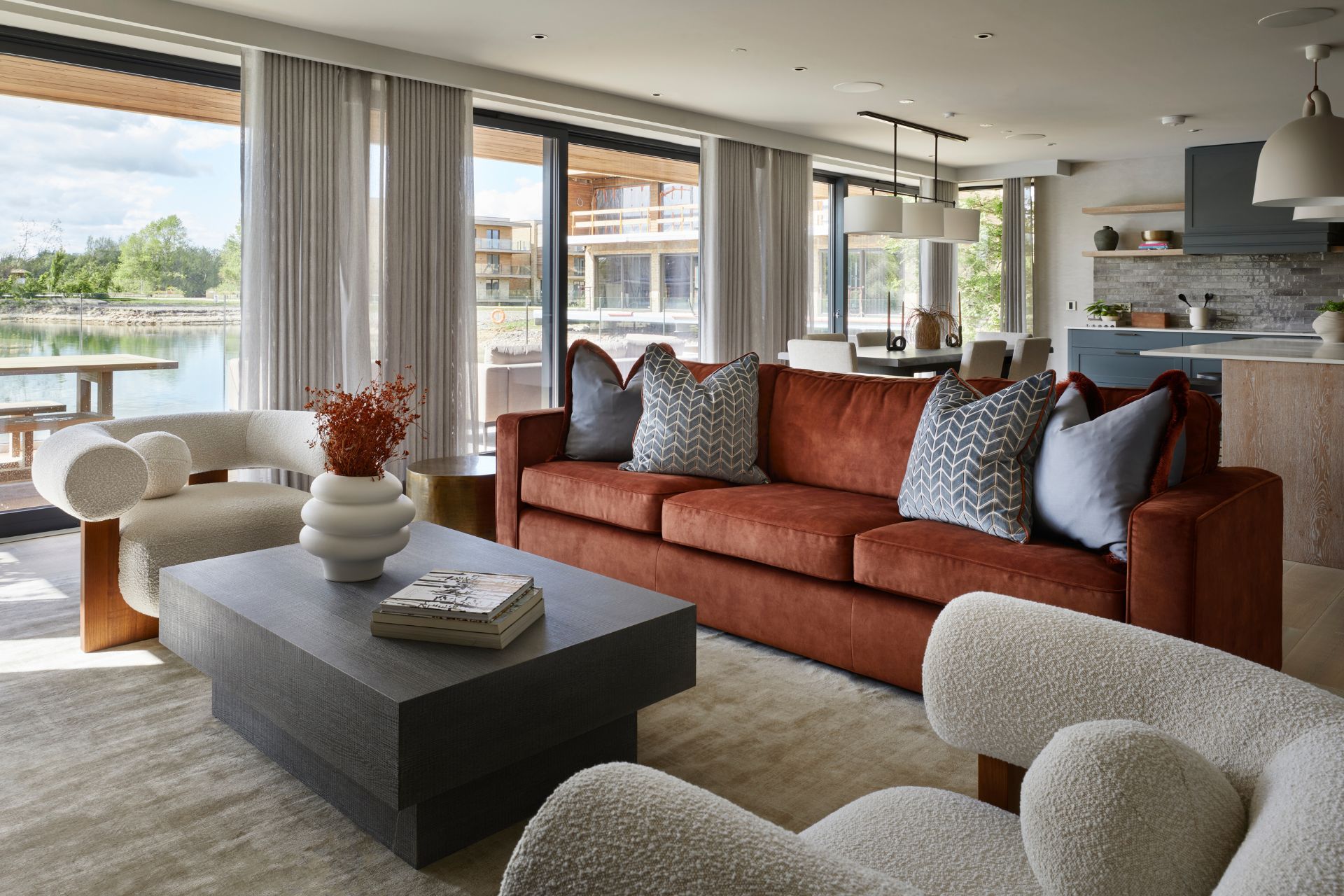 Lakeside living room with burnt orange velvet sofa, cream boucle armchairs, and a black coffee table.