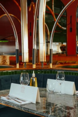 Restaurant with marble tables, yellow crushed velvet seating and brass archways.