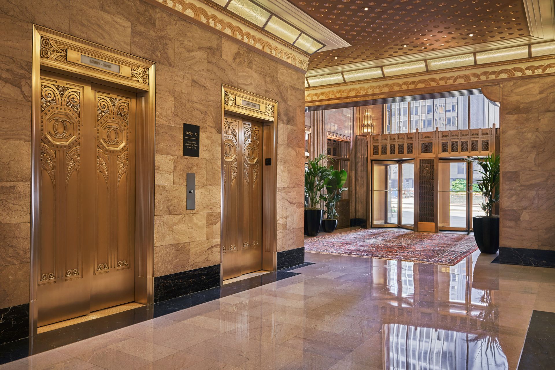 Art Deco style hotel lobby with gold elevators, marble floors and gold ceilings.