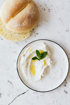 A bowl of cottage cheese beside a bread roll