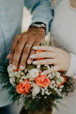 Bride and groom holding hands over a bouquet of flowers on their wedding day