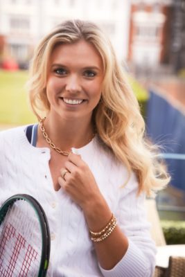 Katie Boulter wearing a white sweatshirt and gold Pragnell jewellery, holding a tennis racquet.