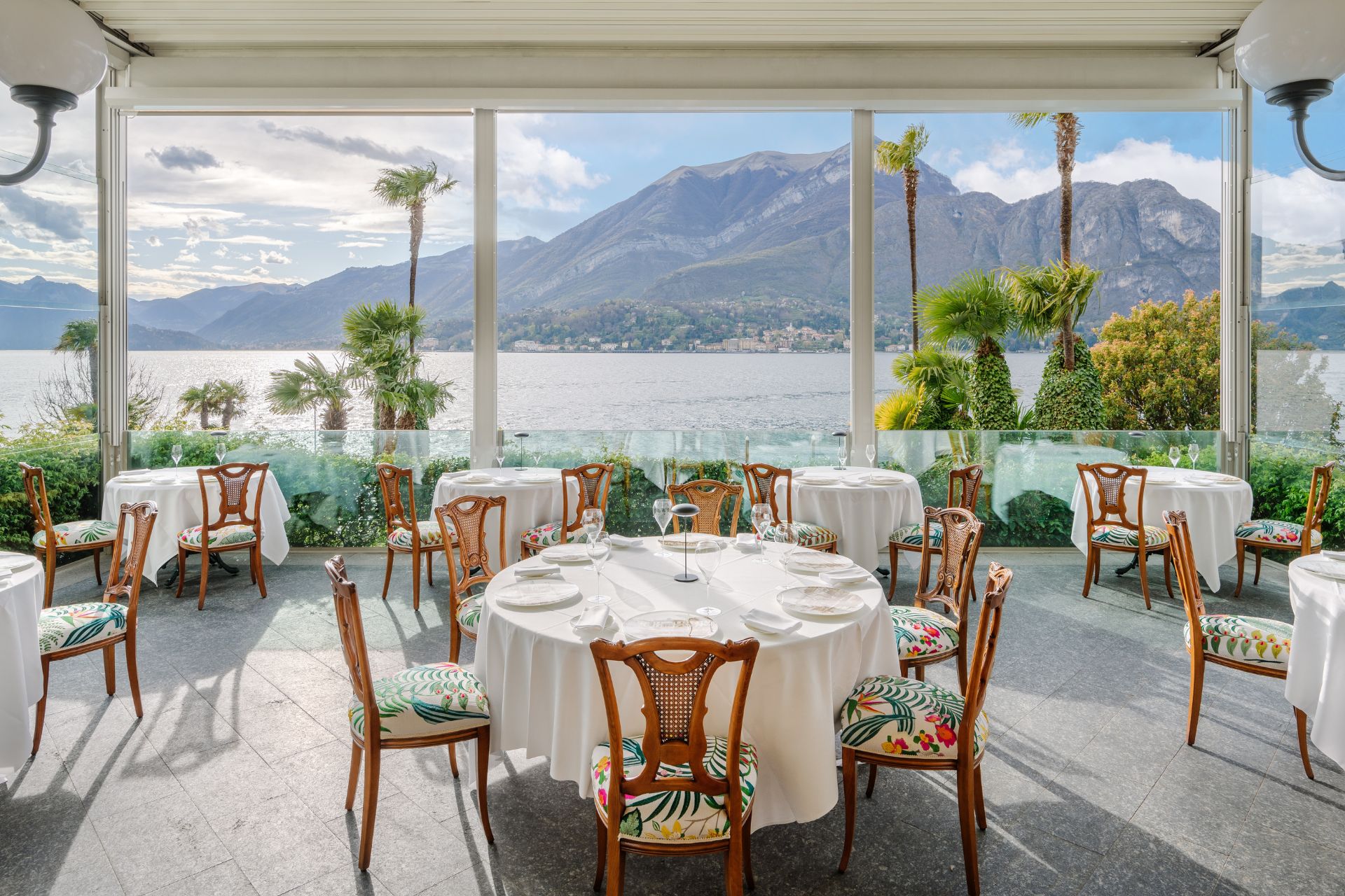 Restaurant with wooden chairs, white tablecloths and floor-to-ceiling windows overlooking Lake Como.