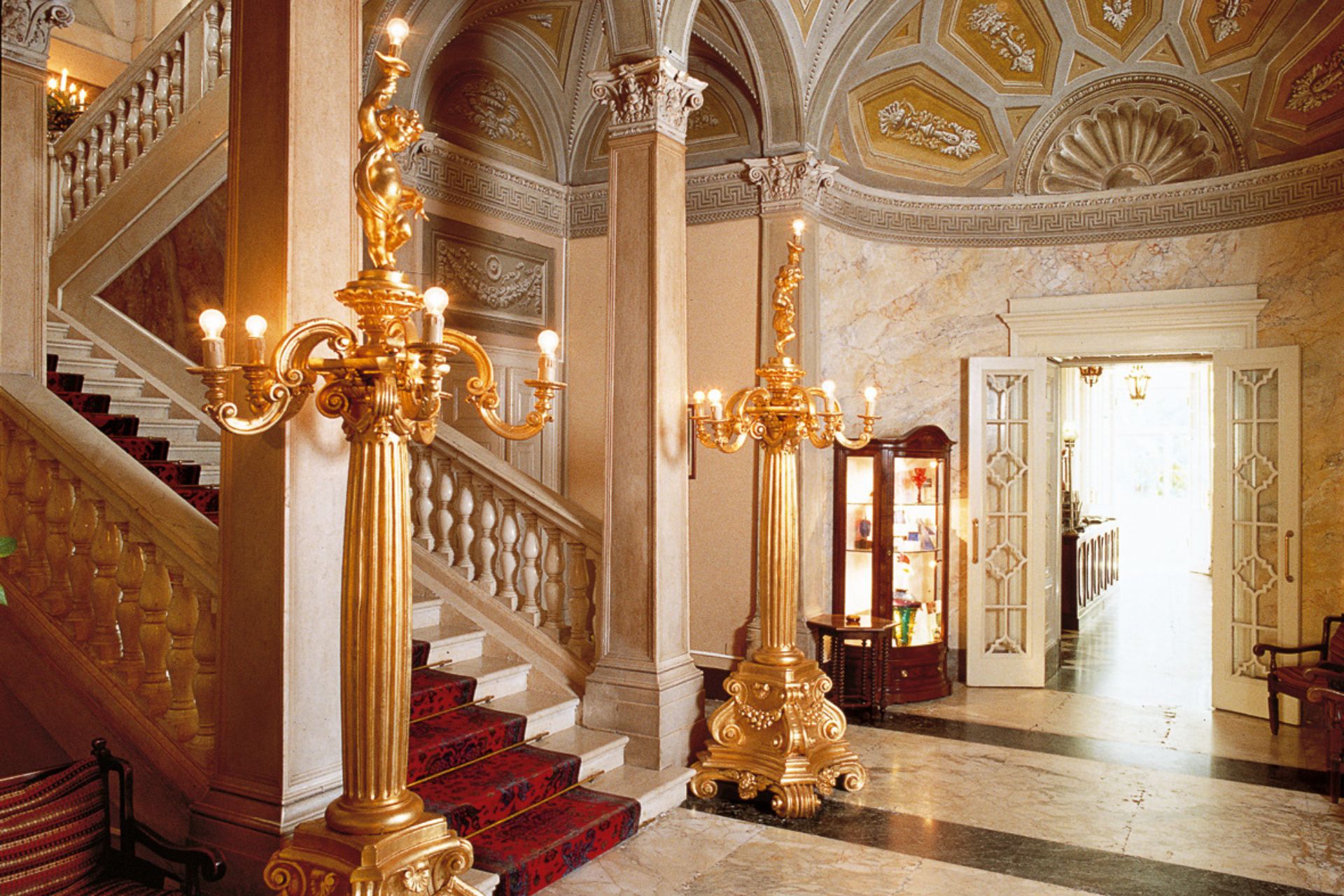 Lobby with a grand staircase, ceiling frescoes and chandeliers.