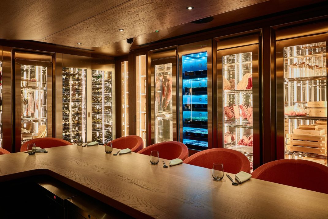 Chef's table with red dining chairs, a dark walnut table and glass-panelled fridges lining the walls.