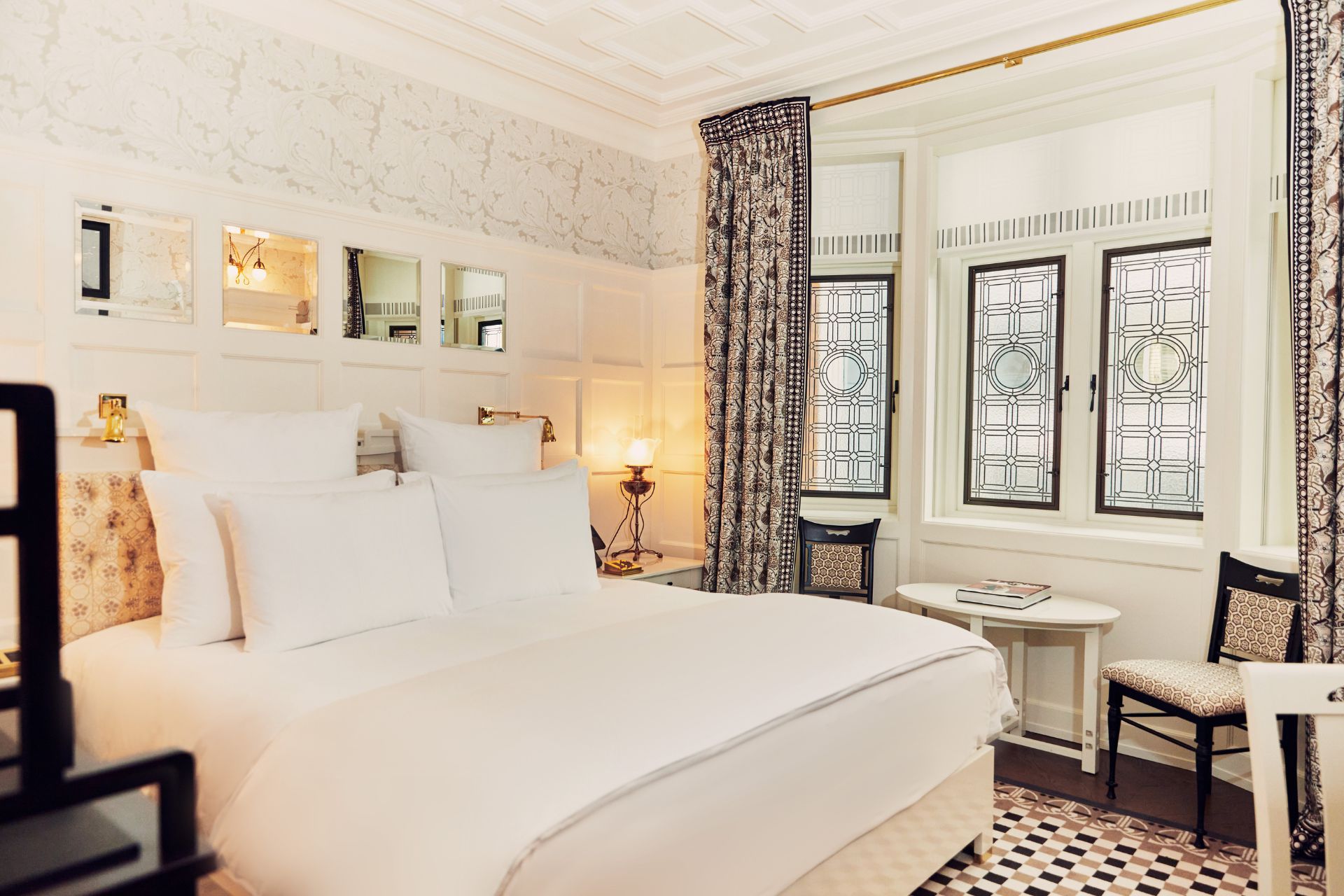 Hotel bedroom with white walls, cornicing, a stained glass bay window and black and white patterned curtains.