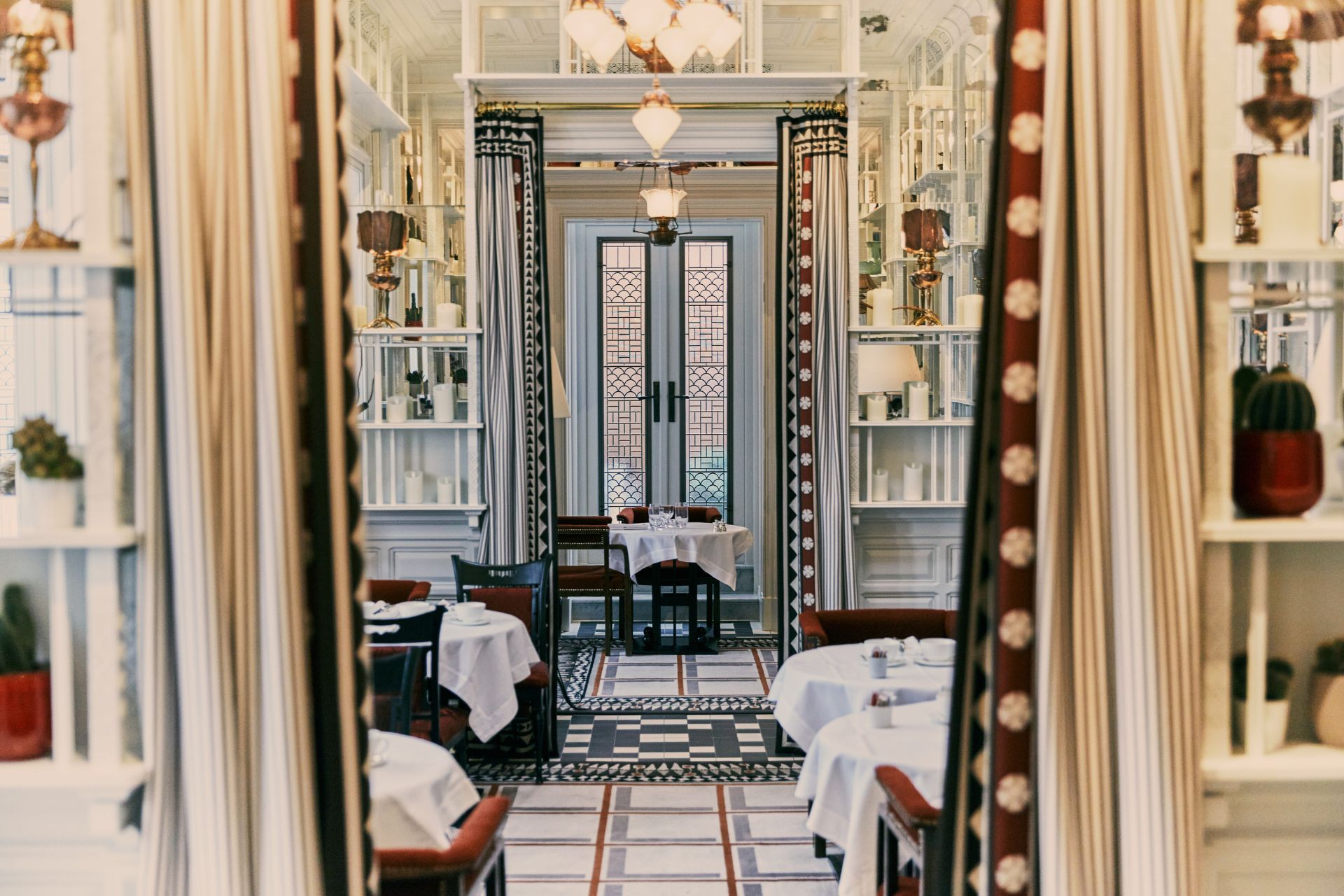 Hotel restaurant with floral wallpaper, red drapes and white tablecloths.