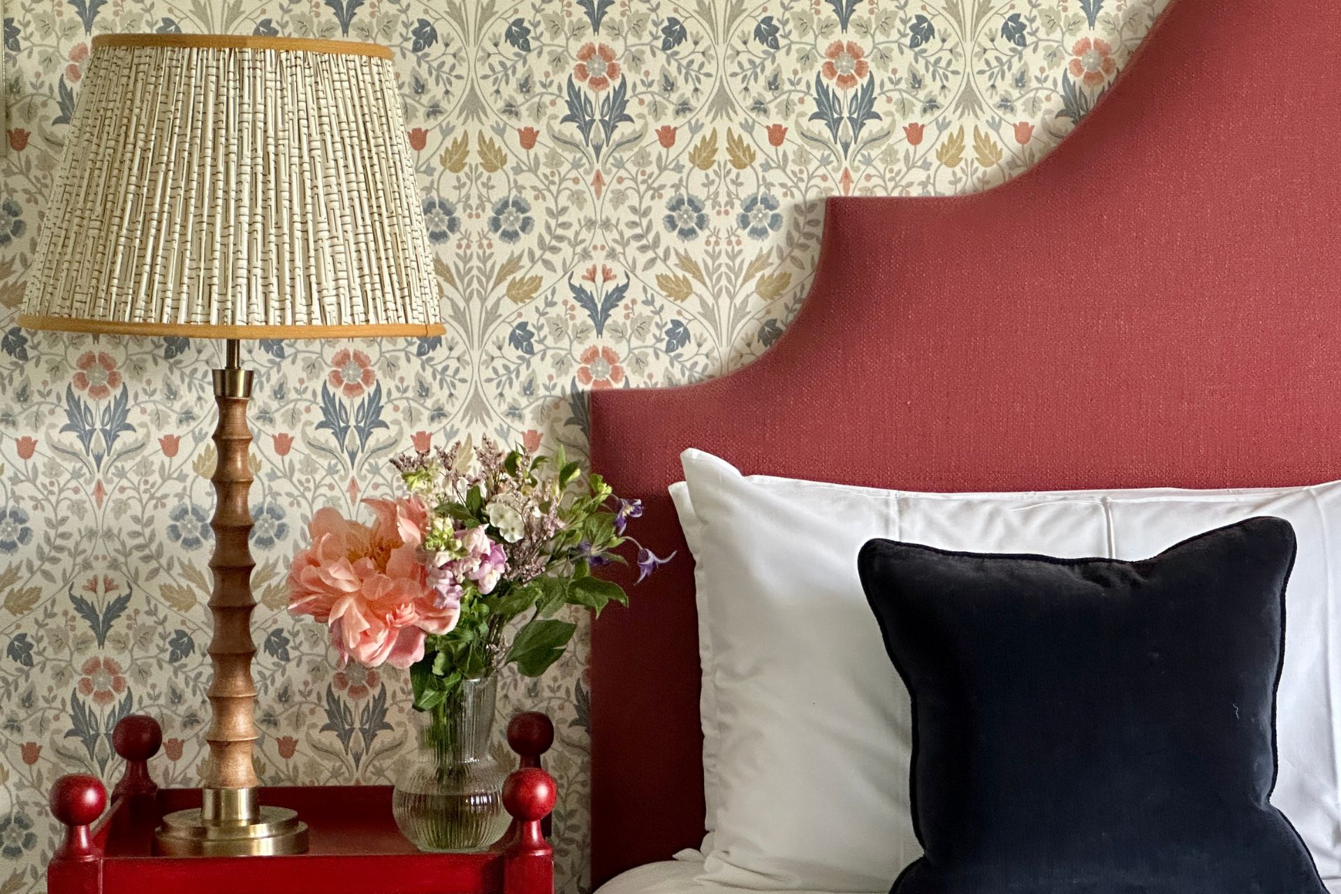 Bedroom with red headboard, black cushion and floral wallpaper.