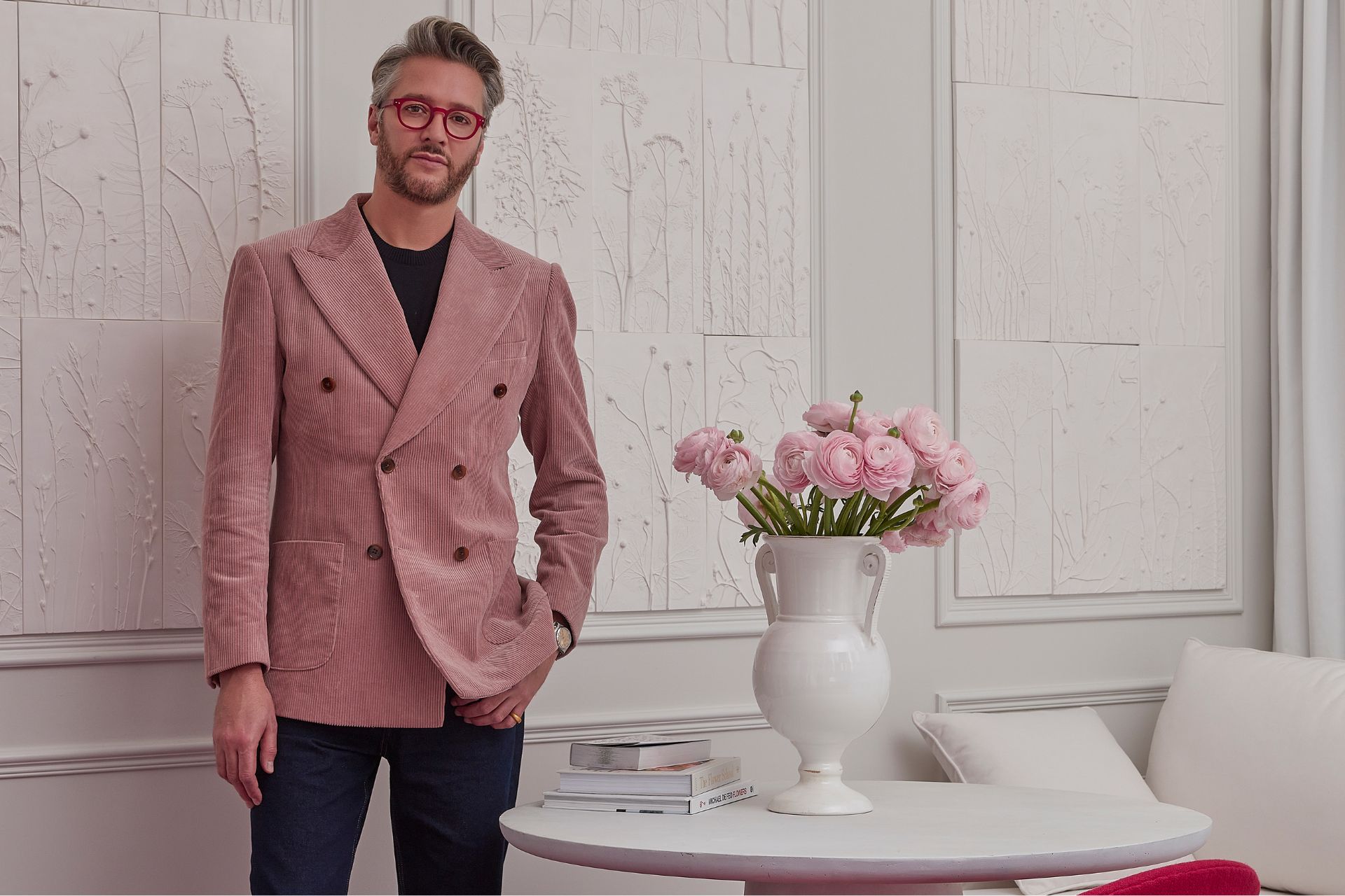 Designer Jacu Strauss wearing a powder pink blazer in a white hotel room with a vase of pink tulips