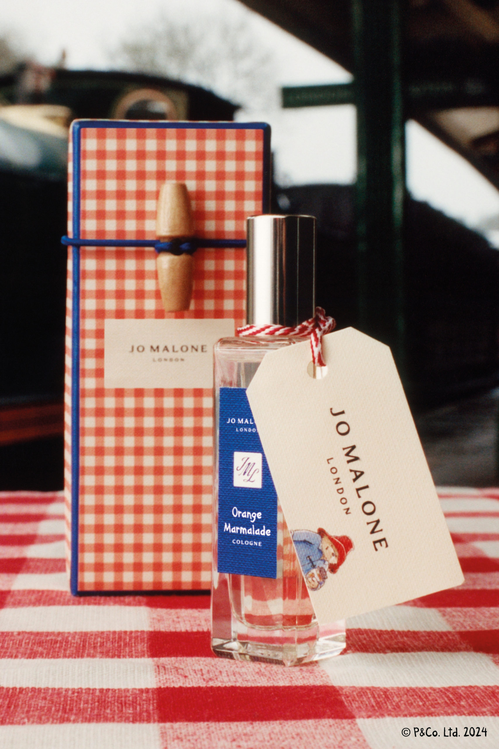 Bottle of cologne next to red check box, set on matching tablecloth