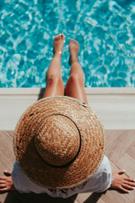 A woman in a summer hat with her feet in a swimming pool