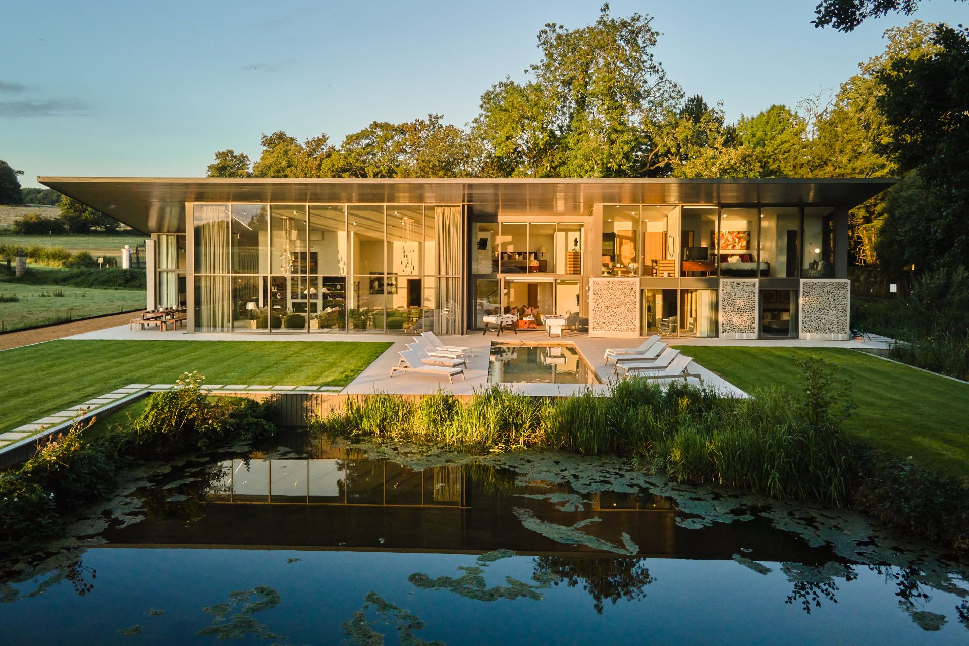 Large contemporary house with floor-to-ceiling windows, an outdoor pool, and a lake.