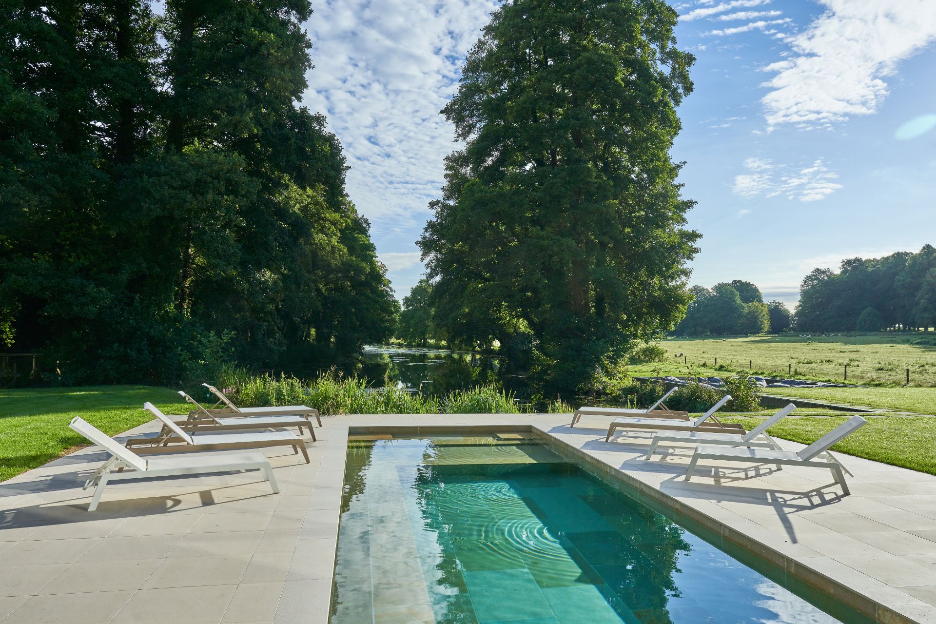 Outdoor pool area with sun loungers and a lake