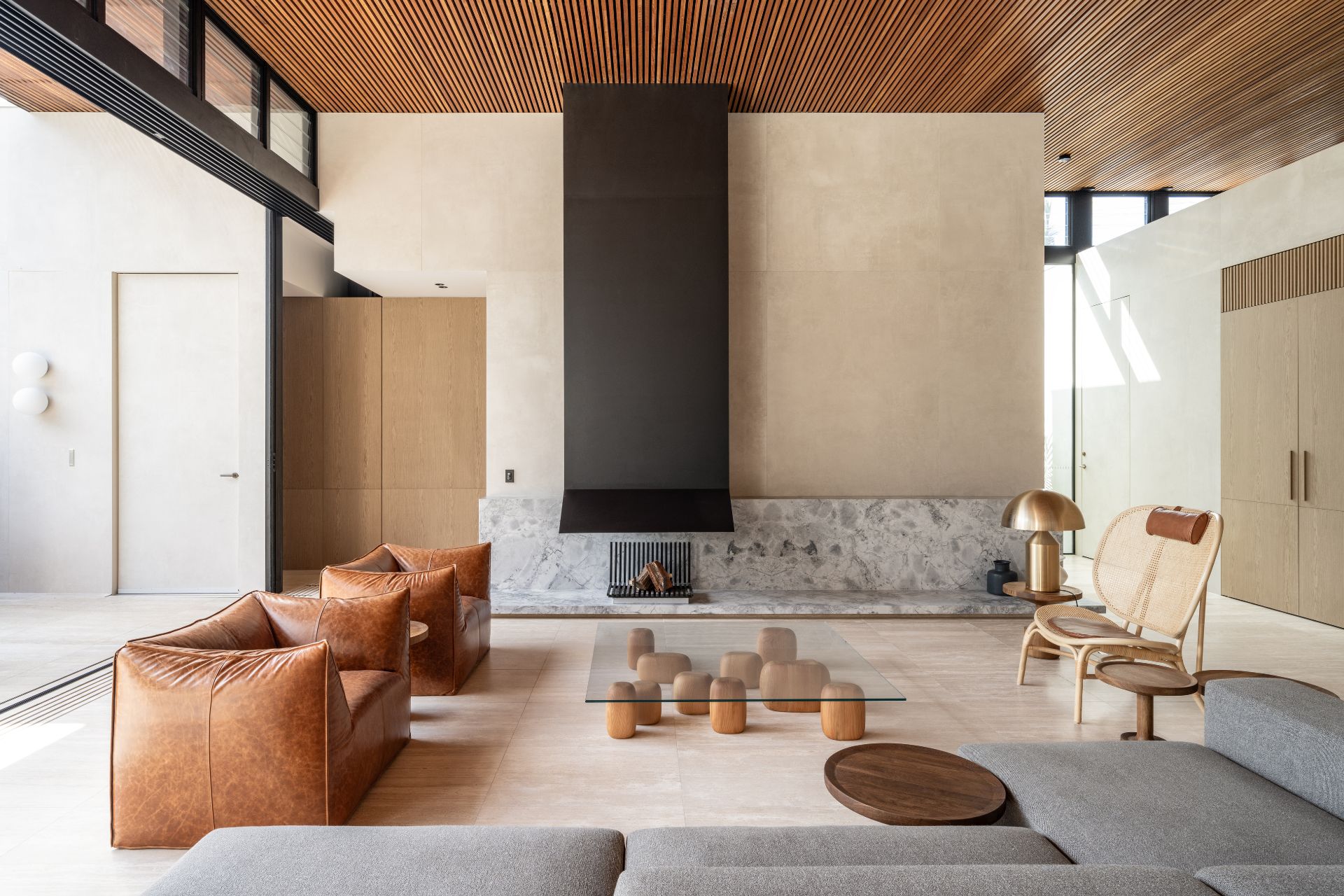 Living room with marble wall panel, fireplace, tan leather armchairs and a grey sofa.