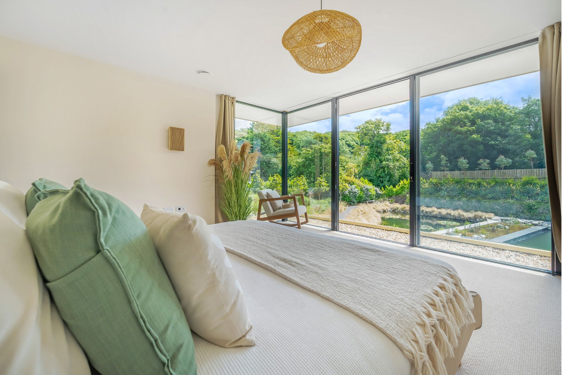 Bedroom with floor-to-ceiling windows overlooking gardens with a pond. 