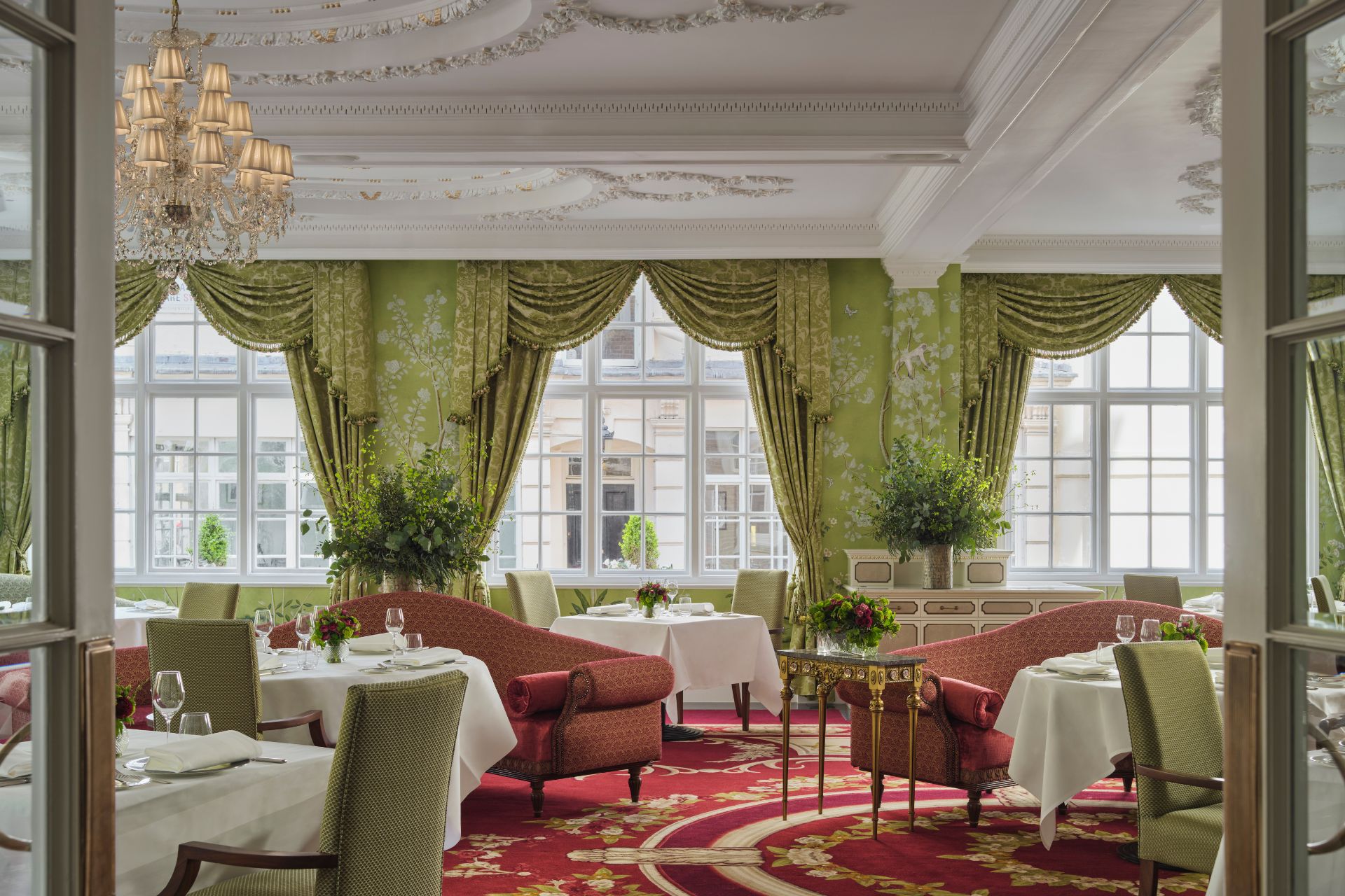 The Dining Room at The Goring, featuring red carpets, green floral wallpaper, green curtains and red sofas.