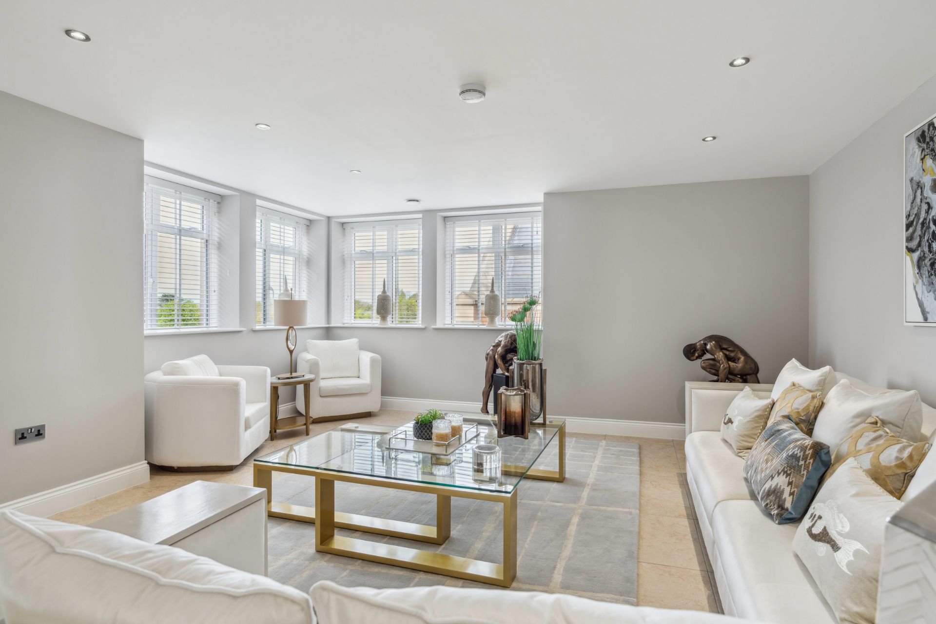 Living room with cream sofas, cream armchaors and a glass coffee table with gold legs.