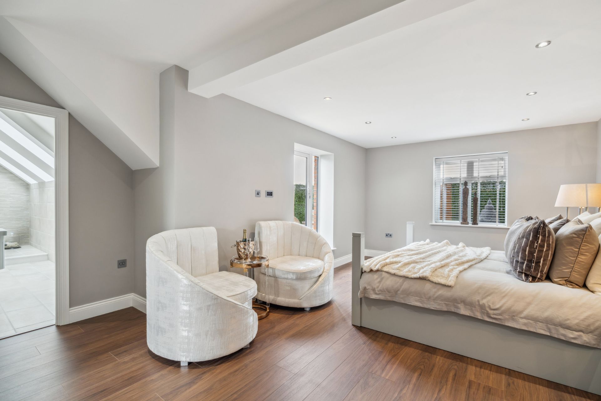 Bedroom with cream armchairs, en suite bathroom and gold cushions.