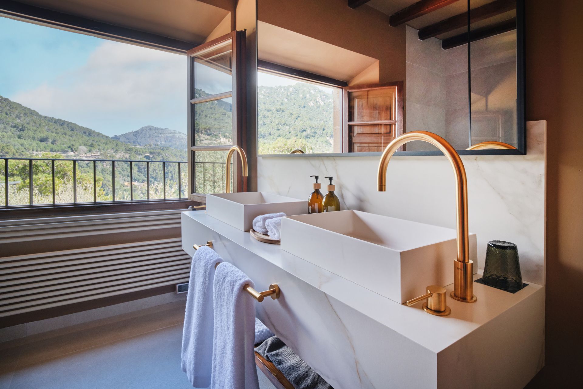 Bathroom with marble sink, gold tap and mountain views.