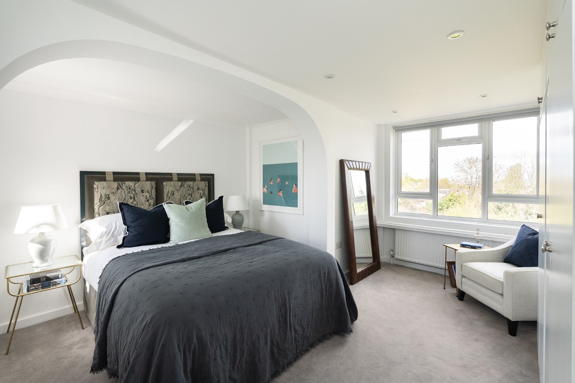 Bedroom with navy bedspread, white armchair and full-length mirror