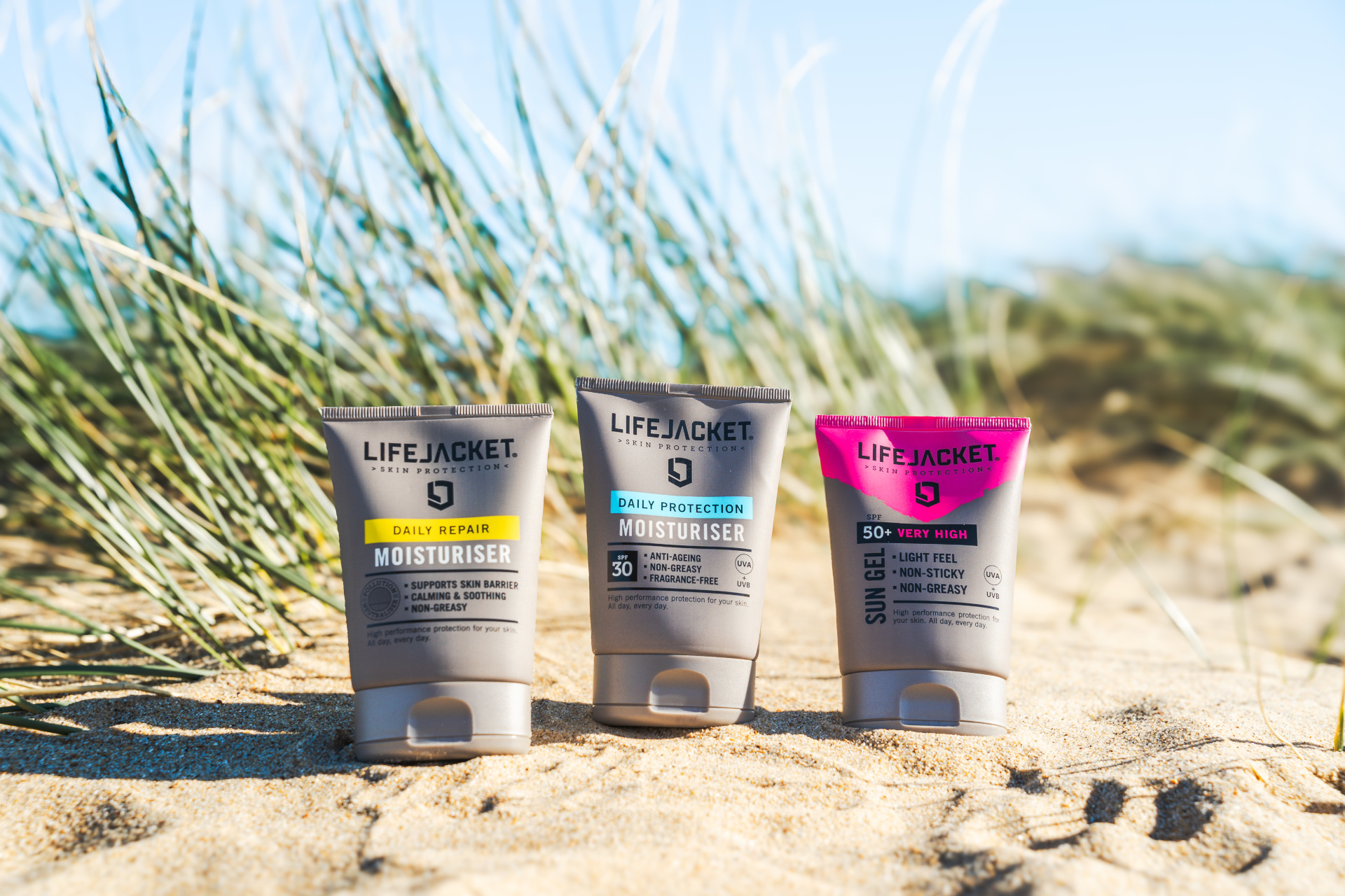 Three skincare bottles in sand