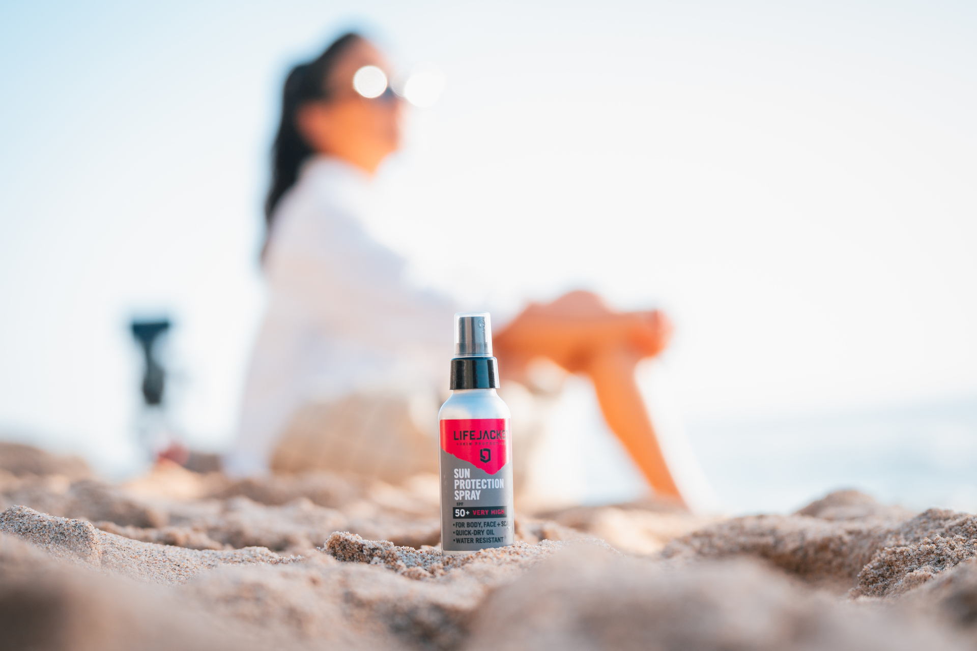 Skincare product in sand with woman out of focus in background