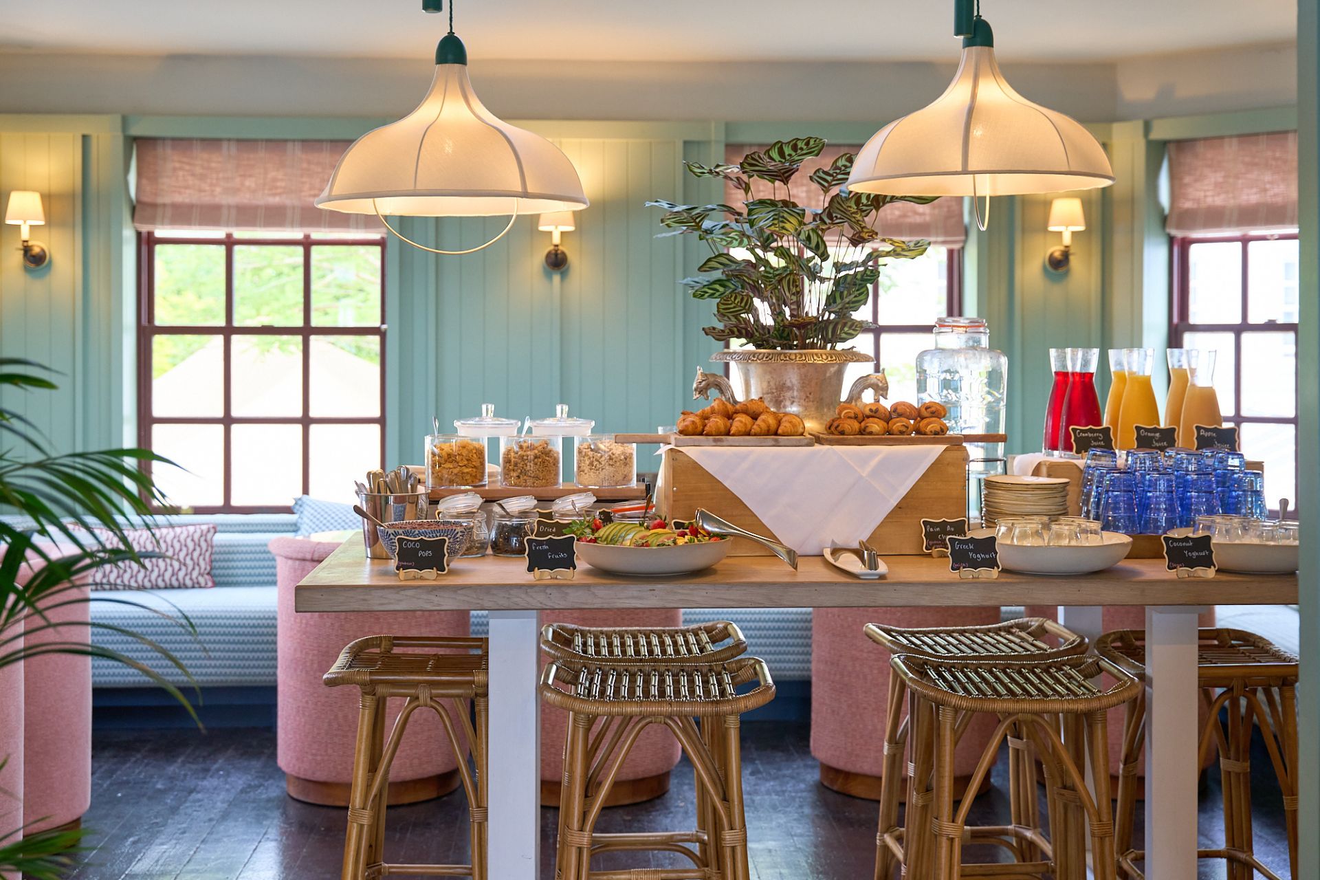 Pastel green panelled restaurant with pink chairs and a breakfast buffet.