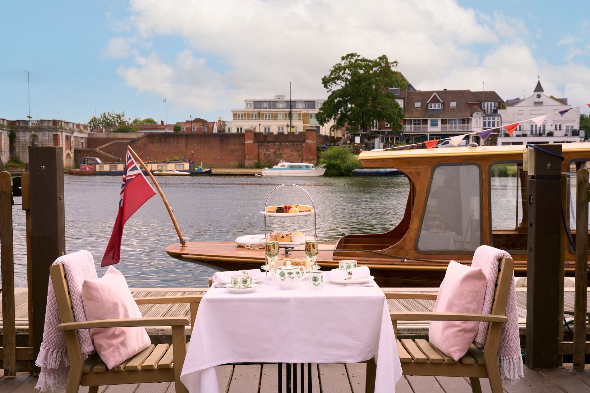 Terrace with pink chairs, white tablecloths and an afternoon tea spread.