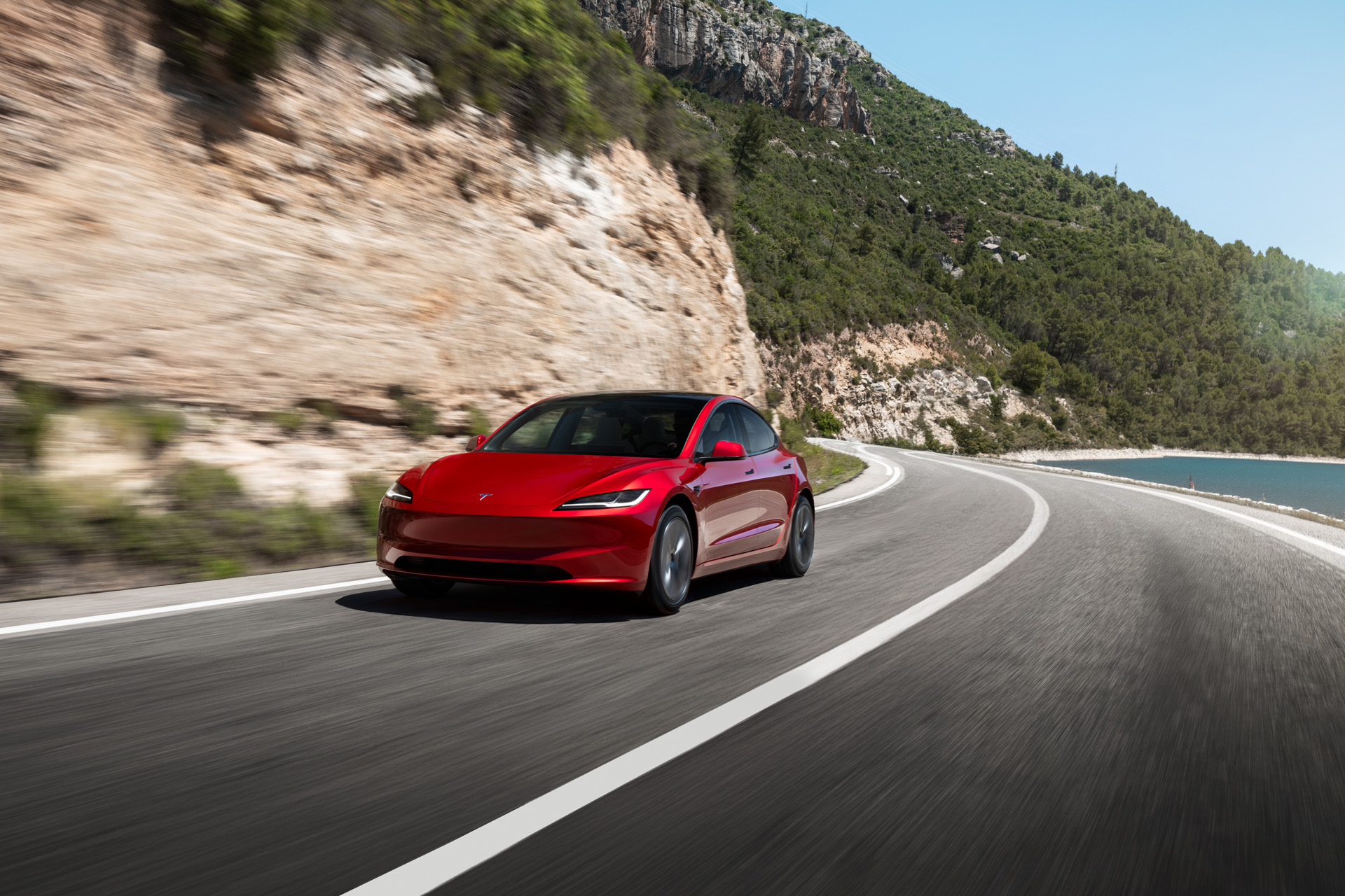 Red Tesla Model 3 on a coastal road