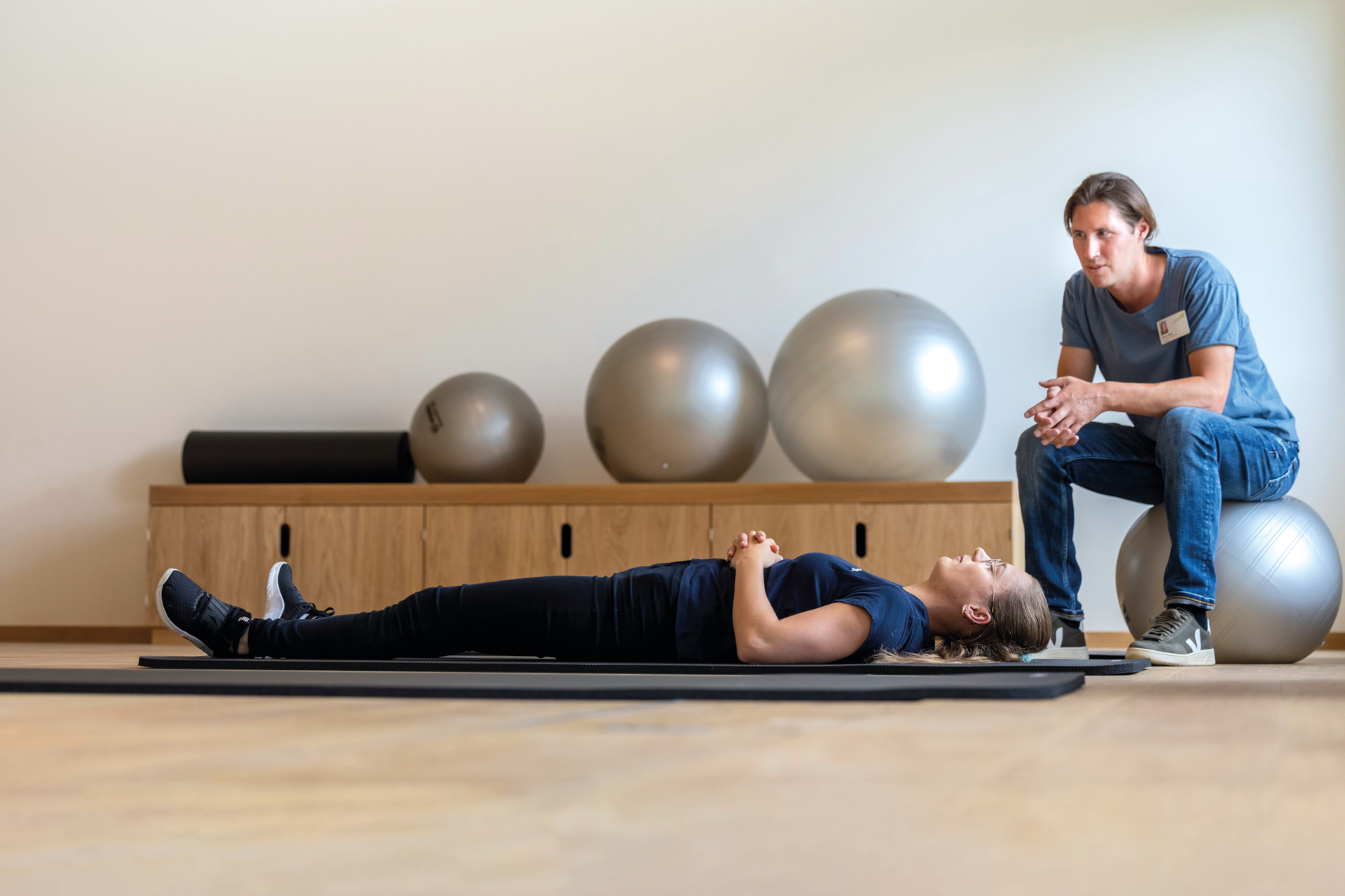 Woman lying on mat with male instructor sat next to her | Switzerland Health Clinics