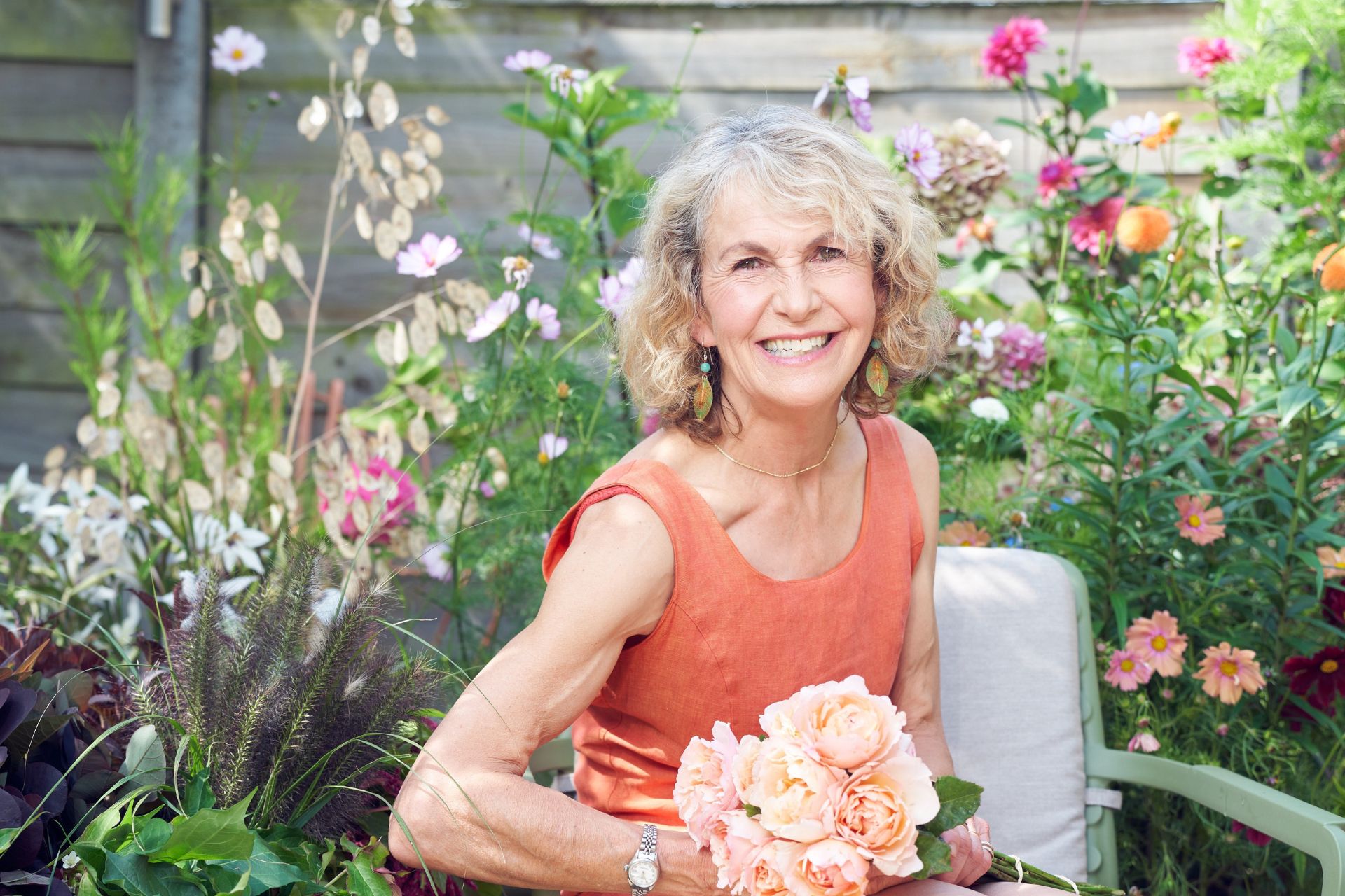 Rosebie Morton wearing a red linen dress and holding a bouquet of pink flowers.