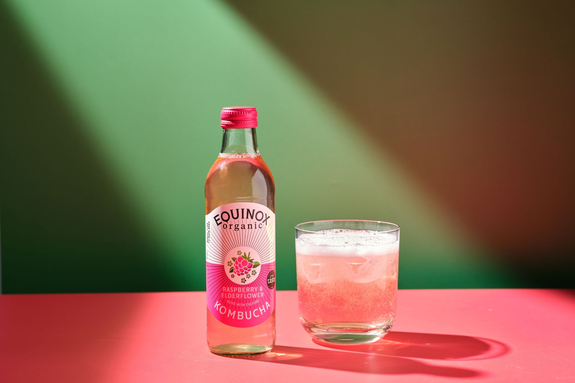 Glass bottle of raspberry and elderflower kombucha against a green background