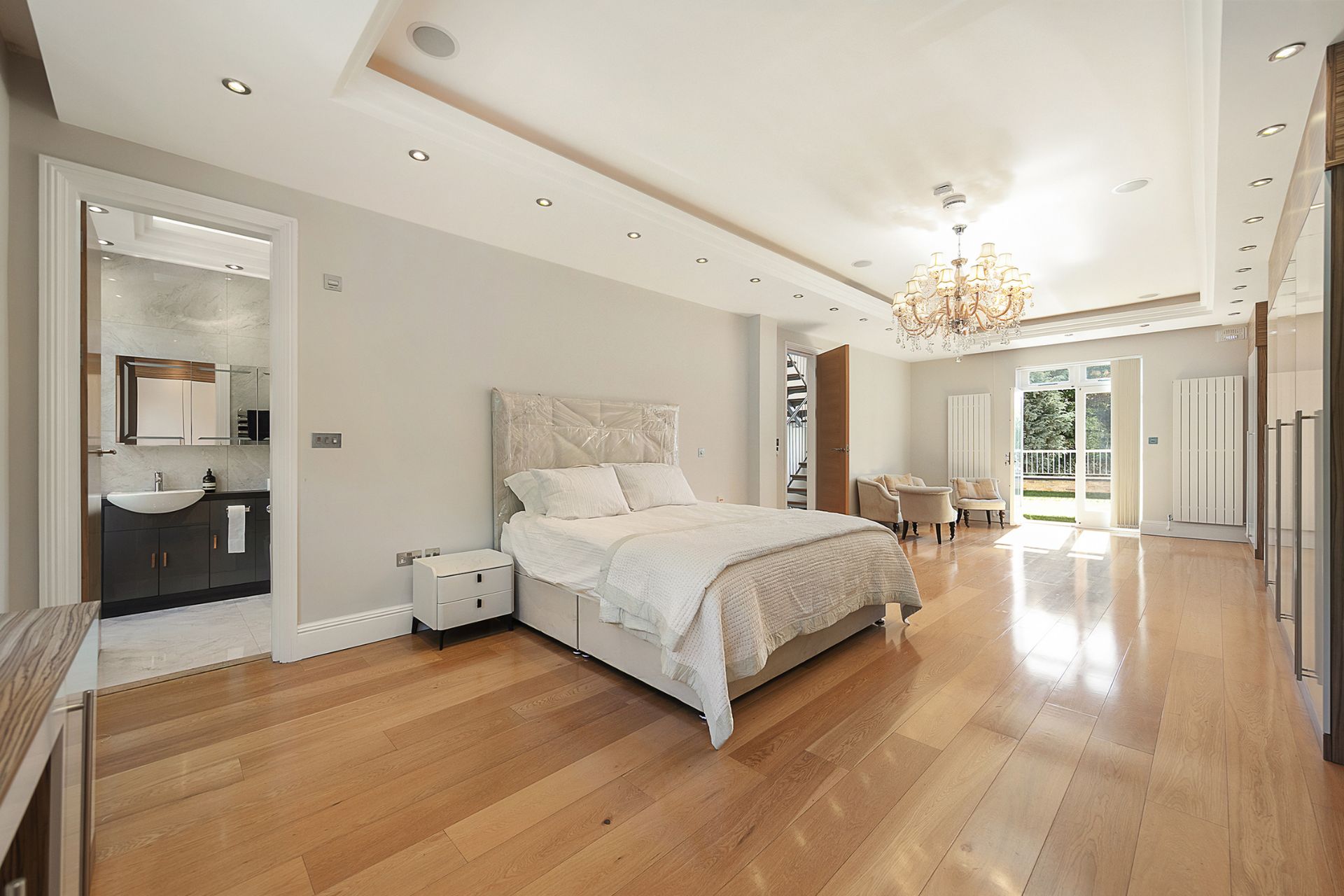 Large bedroom with wooden floors, chandelier and arched windows.