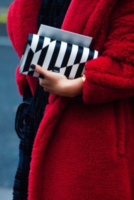 Close up of person in red coat holding black and white stripe clutch bag | fashion podcasts
