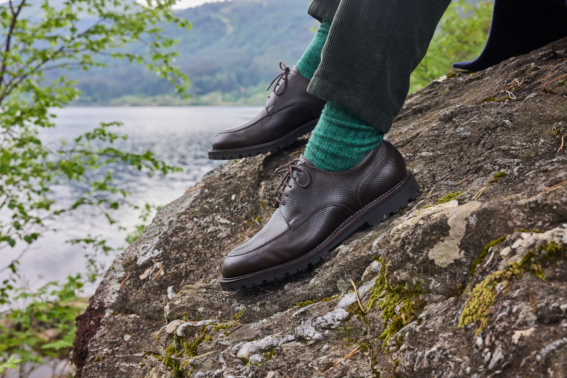 Close up of feet in shoes and green socks on rock by lake