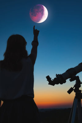 Girl looking at lunar eclipse through a telescope.
