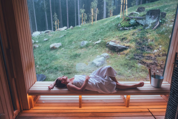 Woman lying in an outdoor sauna by the forest | wellness trends 2025