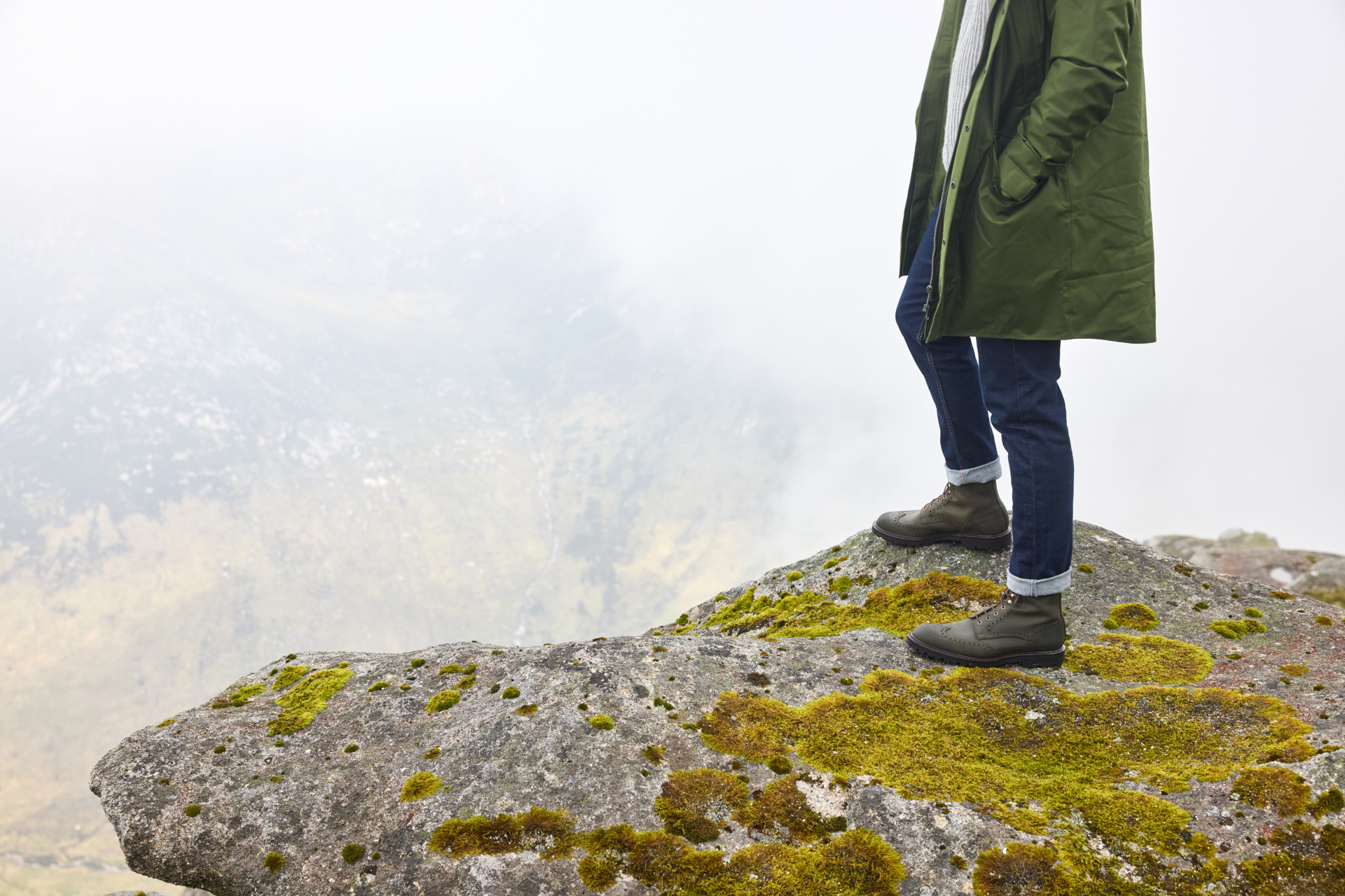 Man wearing country clothing stood on a rock overlooking mountains