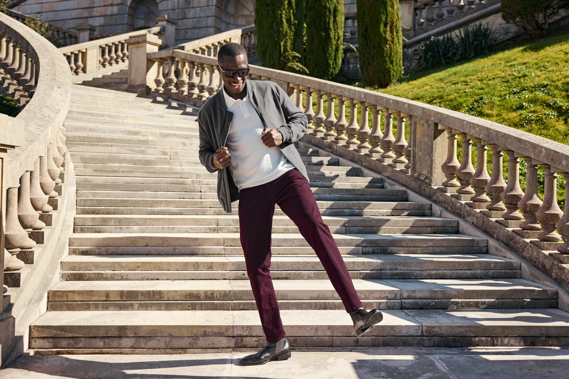 Man in grey cardigan, white top and red trousers