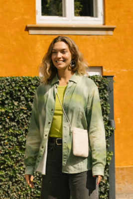 Woman with tailored midi cut wearing green top, stood in front of hedge and orange building