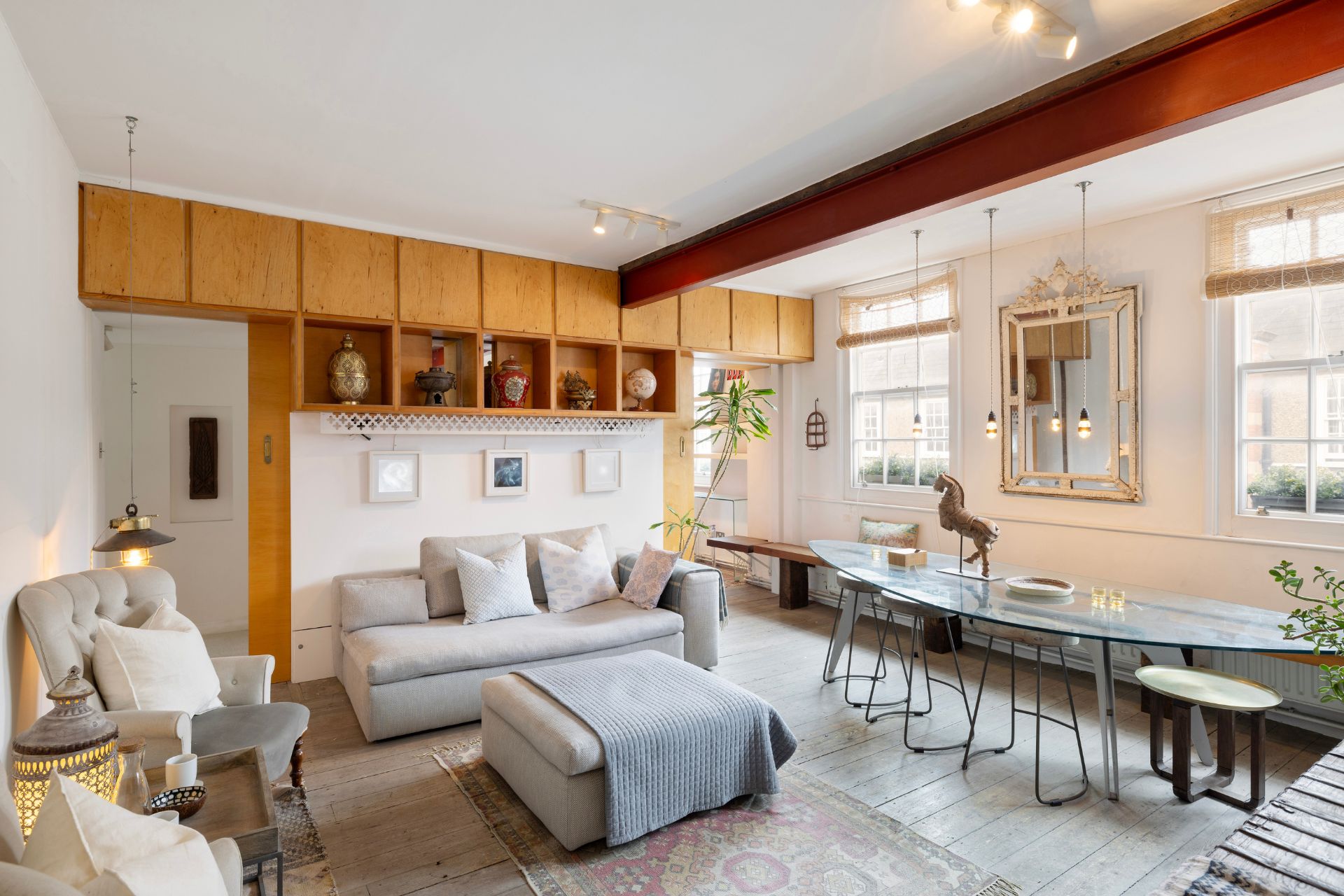 Living room with built-in wooden cupboards, grey sofa and glass dining table.