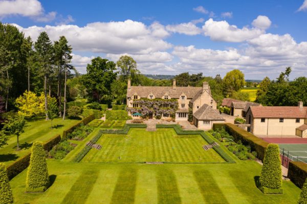 Aerial view of wisteria-clad Cotswolds home with landscaped lawns.